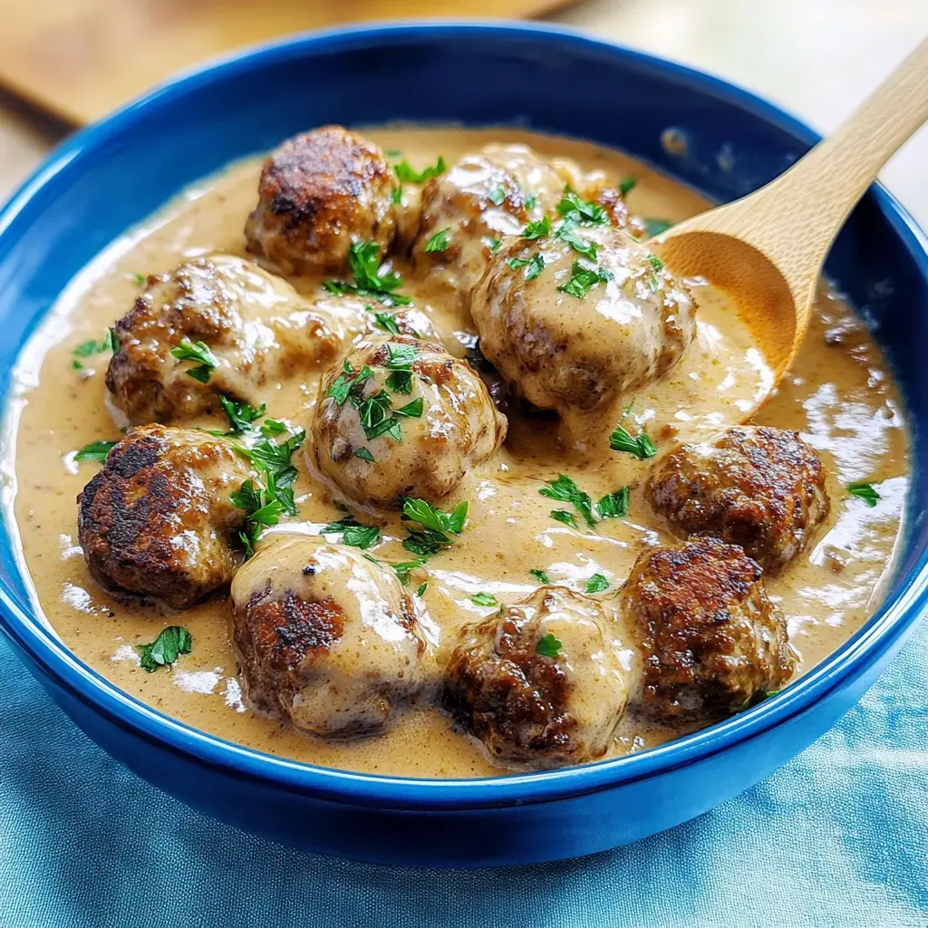 Un bol rempli de boulettes nappées de sauce crémeuse, avec une touche de persil frais.
