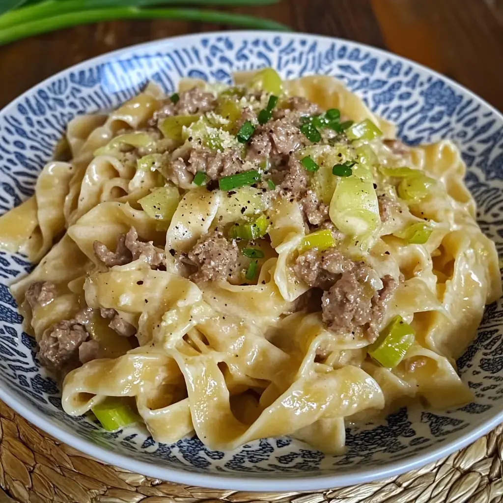 Un bol appétissant de tagliatelles avec viande hachée, verdure et copeaux de parmesan dans une sauce crémeuse.