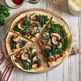 A pizza with mushrooms and kale on a wooden board.