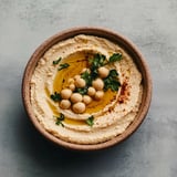 A bowl of houmous with a sprig of parsley.