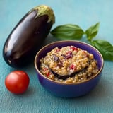 A bowl of food with a tomato and a green vegetable.