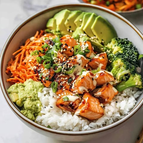 Un bol rempli de riz, laxs doré, carottes râpées, brocolis, avocat tranché, graines de sésame et sauce onctueuse.