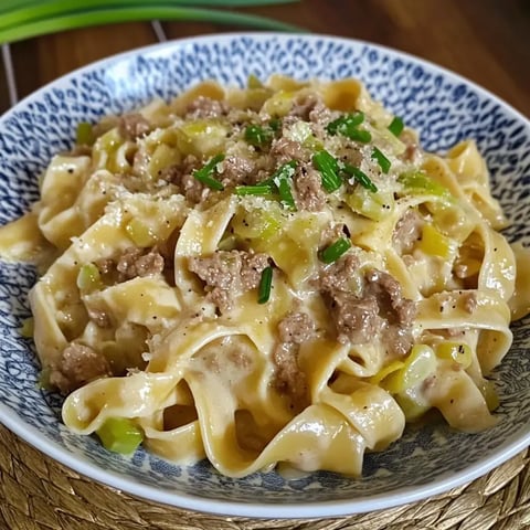 Une assiette de tagliatelles nappées de sauce crémeuse, garnies de bœuf haché, poireaux, ciboulette fraîche et copeaux de parmesan.