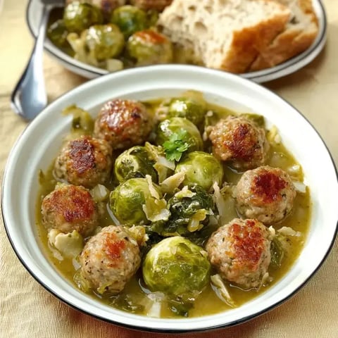 Une assiette remplie de boulettes, choux de Bruxelles et bouillon maison, servie avec un morceau de pain croustillant.